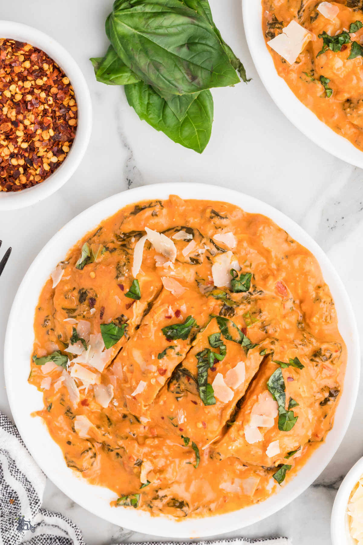 A serving of creamy tomato chicken with kale, basil, and parmesan cheese on a white plate.