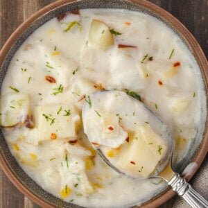 A brown bowl with a spoon filled with fish chowder made with cod fillets and potatoes.