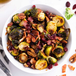 White bowl filled with Caramelized Brussel Sprouts glazed with balsamic vinegar and tossed with cranberries and toasted pecans.
