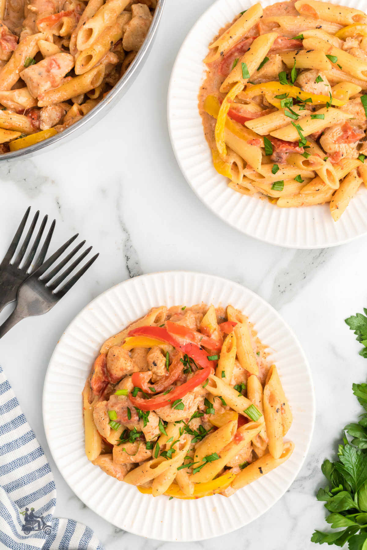 Two bowls filled with creamy cajun chicken pasta with a skillet in the background and Italian parsley on the table. 