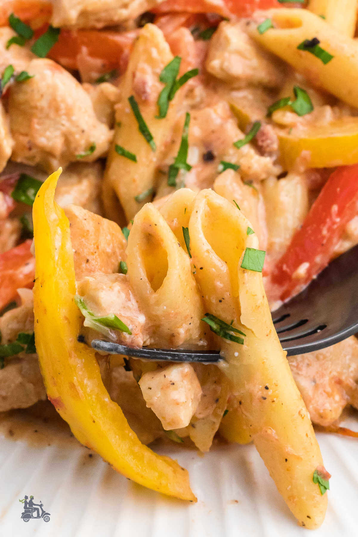 A fork holding a bite of penne pasta, yellow bell pepper slice, and chicken piece from the Cajun Chicken Pasta recipe. 