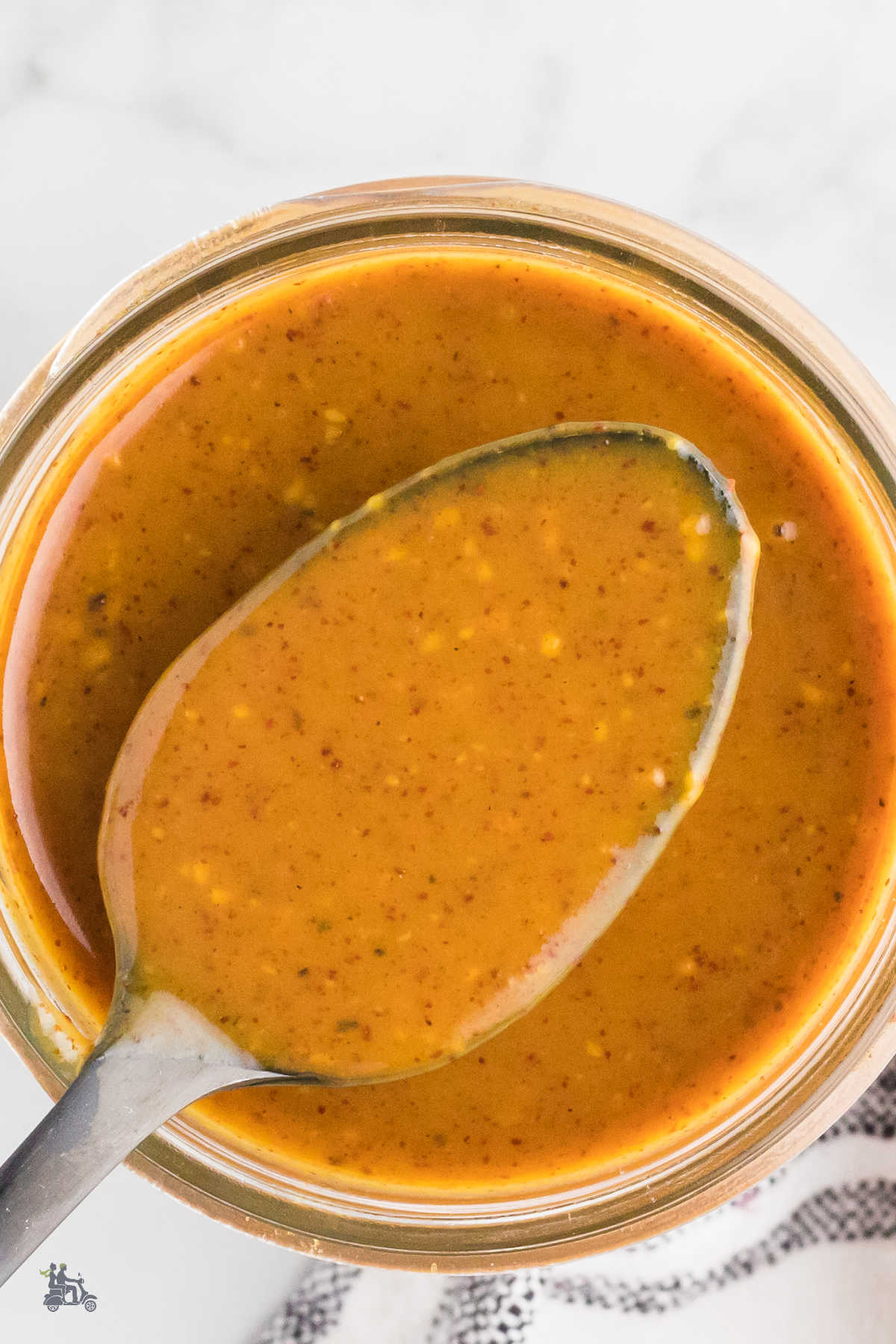 Overhead view of a jelly jar of North Carolina BBQ Sauce with a spoon holding up a sampling of the texture.