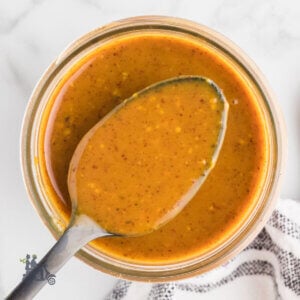 A spoon with a serving of golden North Carolina BBQ Sauce in a jelly jar.