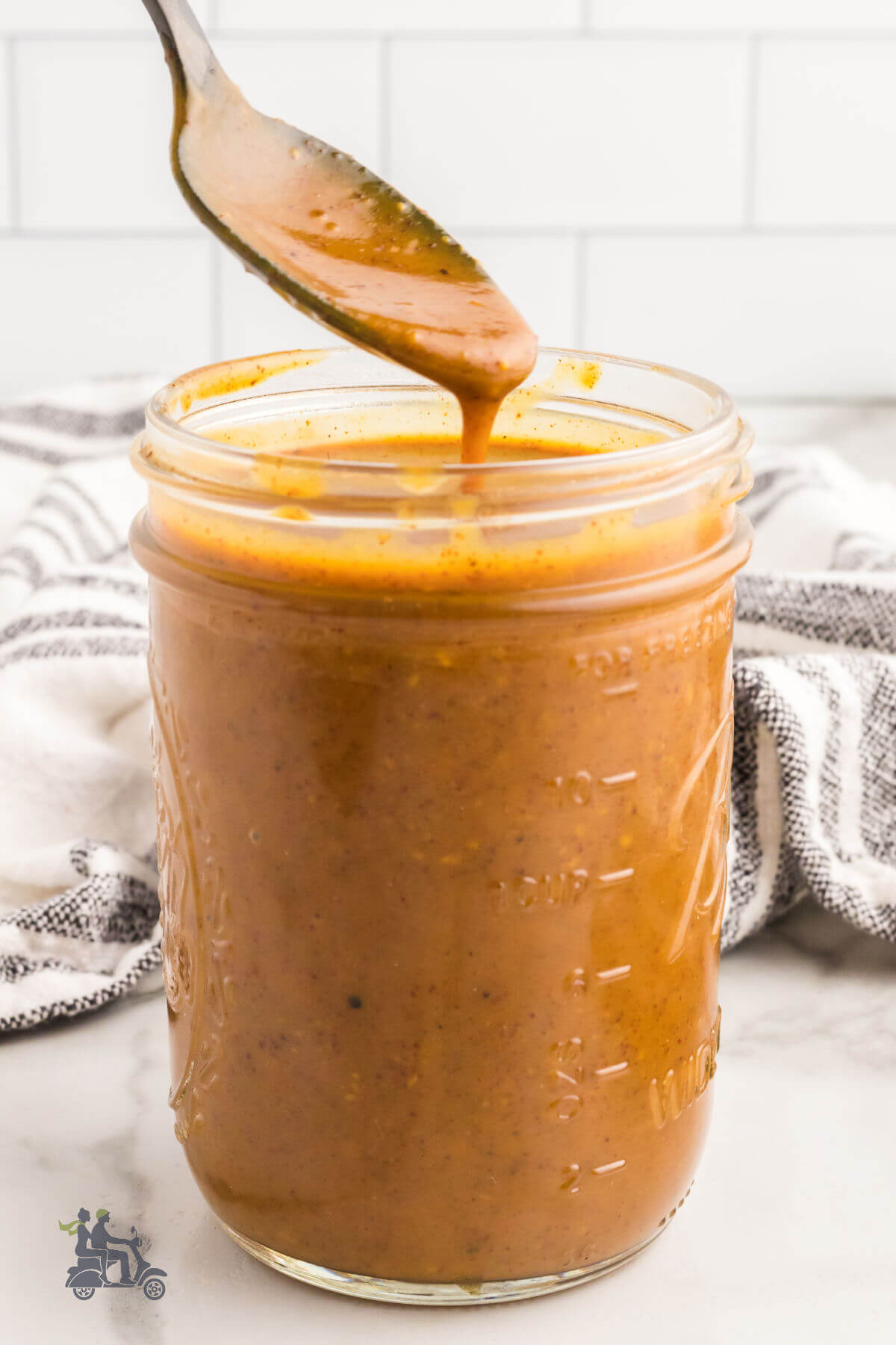 Carolina Barbecue Sauce in a Ball Jar with a spoon dribbling sauce into the jar. 