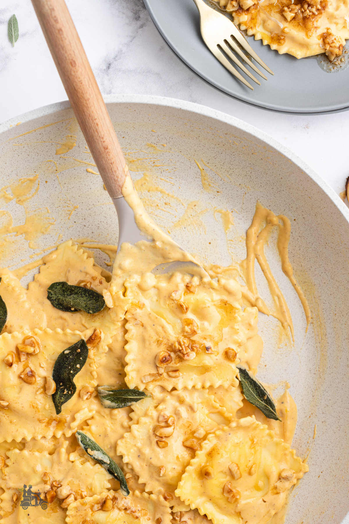 Spoon in a skillet dishing out a serving of pasta with pumpkin cream sauce onto a gray plate. 