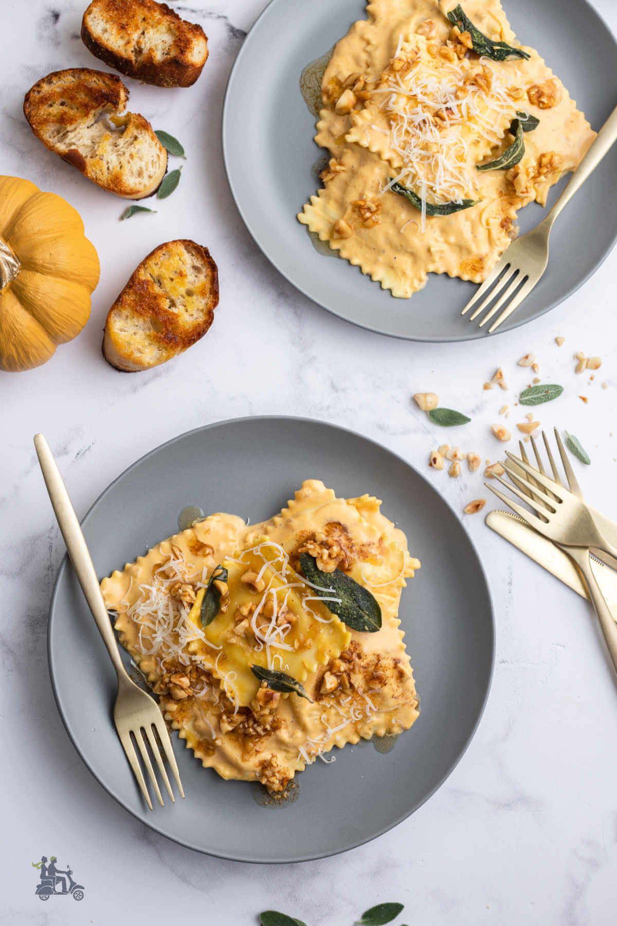 Two gray plates each with a serving of cheese ravioli in pumpkin cream sauce topped with chopped roasted hazelnuts and fried sage. 