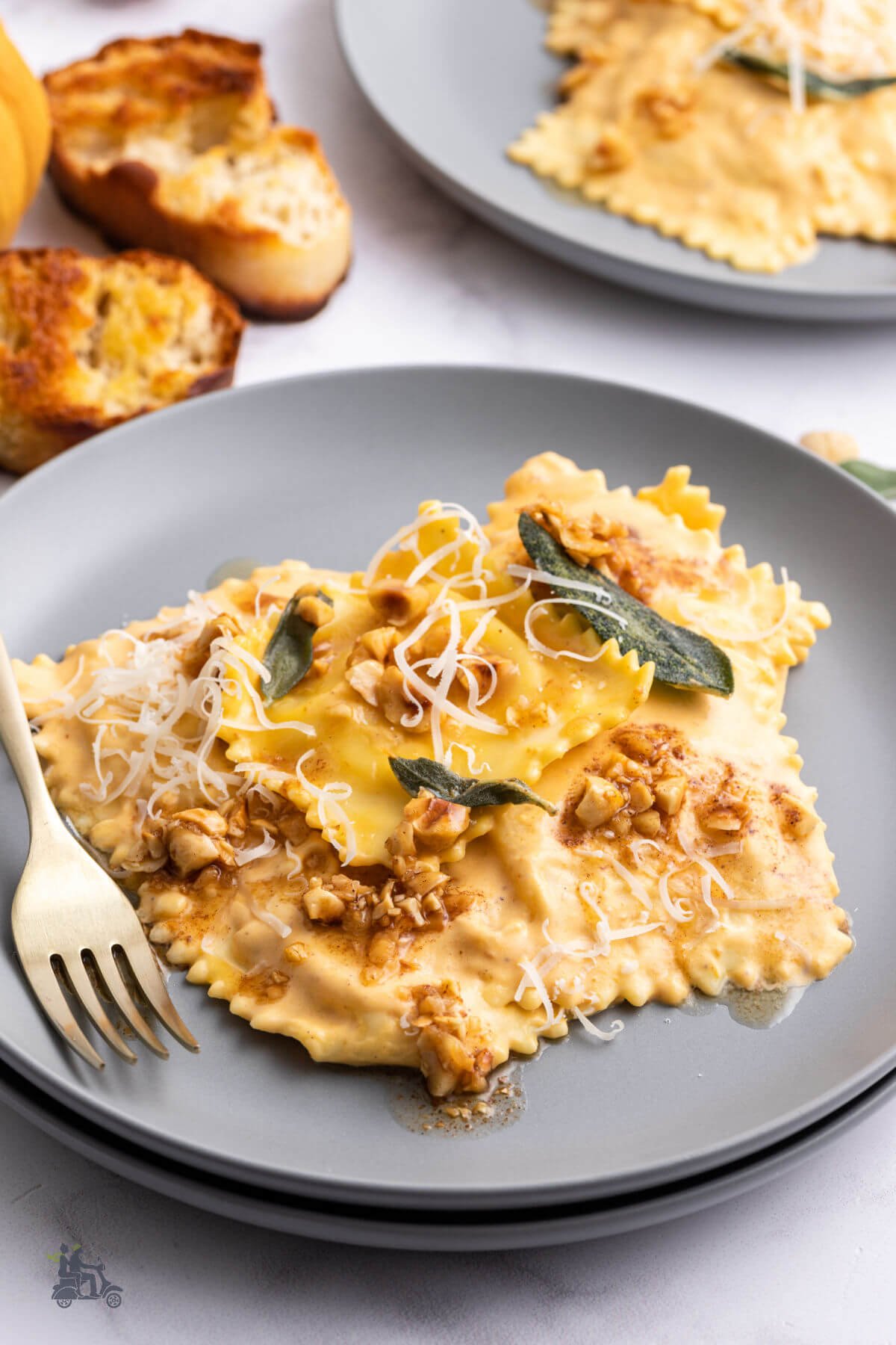 A serving of Cheese Ravioli pasta with pumpkin cream sauce topped with chopped hazelnuts and fried sage leaves. 