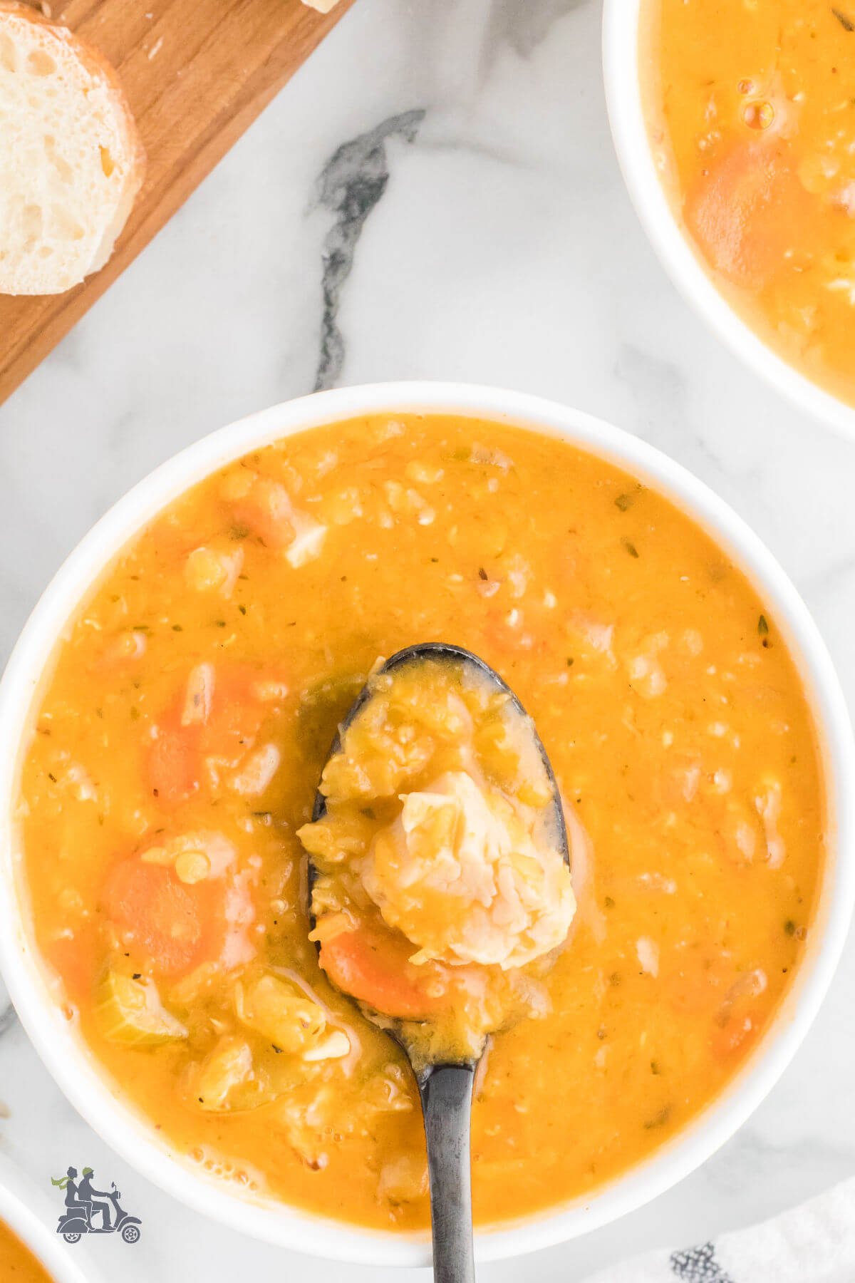 A spoon filled with chicken from a white bowl holding lentil chicken soup. 