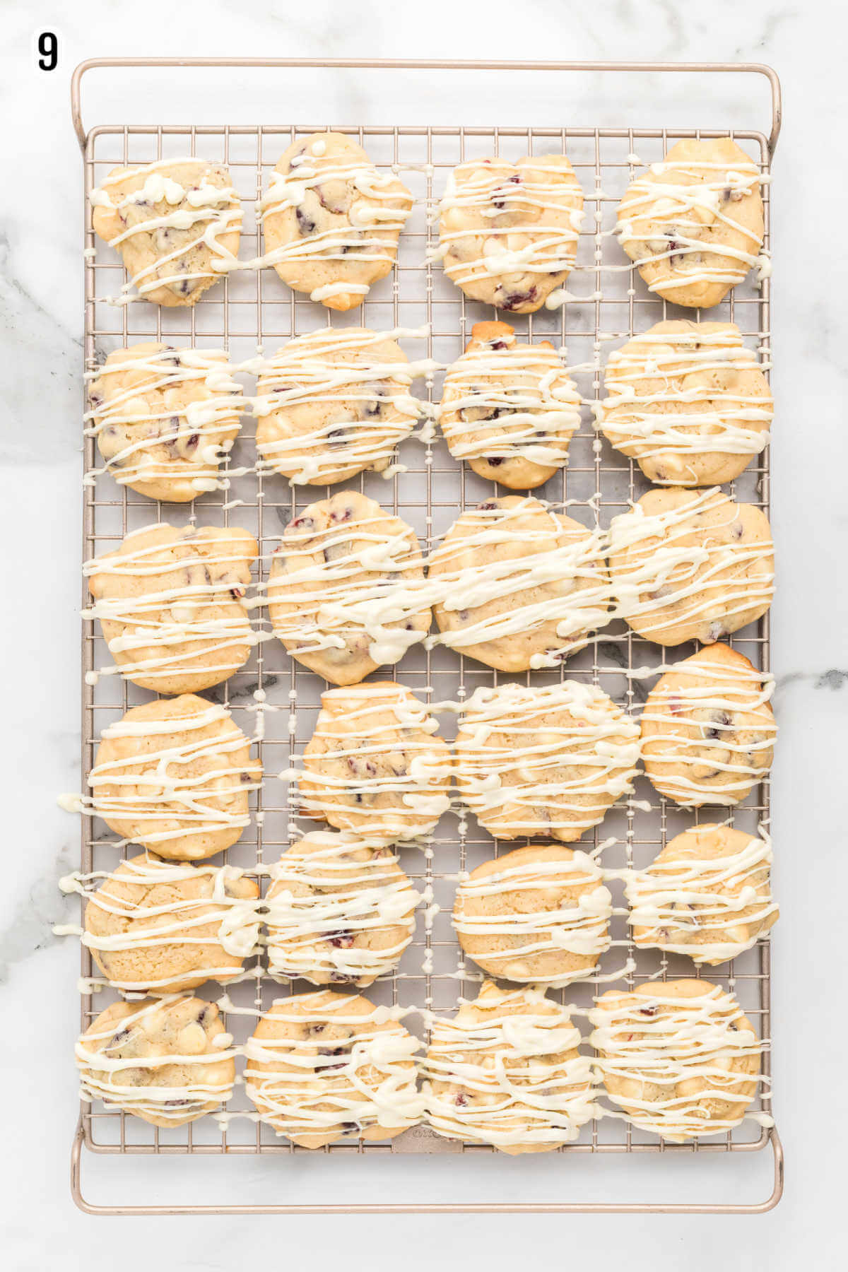 Cranberry White Chocolate Chip Cookies drizzled with white chocolate glaze and drying on a wire rack. 