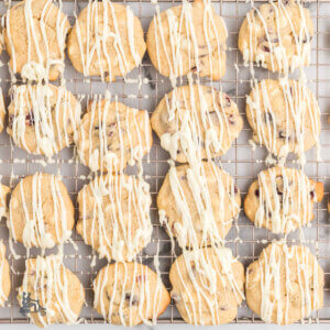 A wire cooling rack holding cranberry white chocolate chip cookies drizzled with white chocolate.
