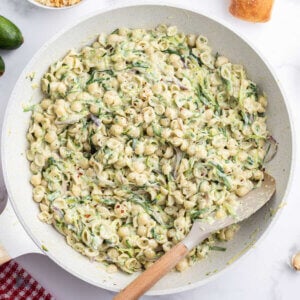 A white skillet filled with creamy zucchini sauce with small pasta shells.
