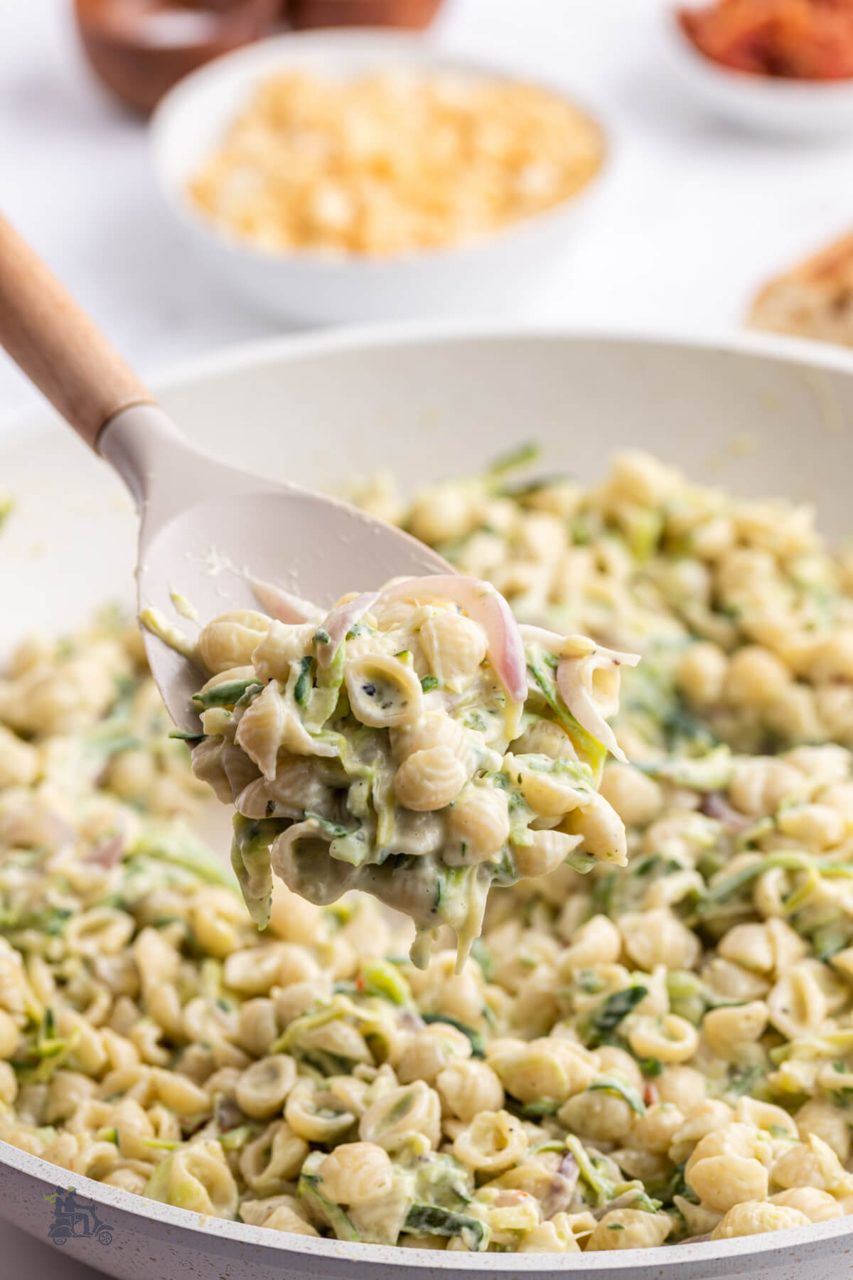 A wooden spoon lifting a spoonful of pasta coated with creamy zucchini sauce. 