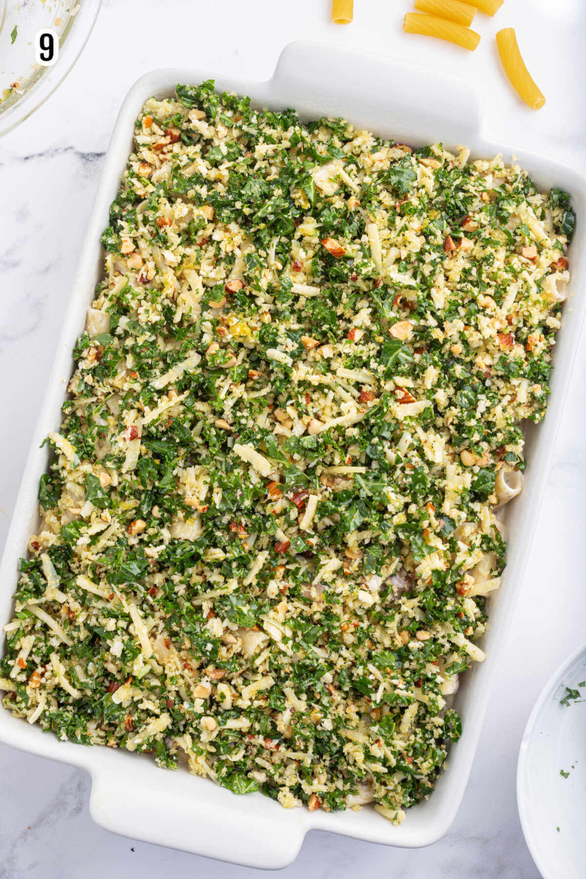 A casserole dish filled with the rigatoni mushroom pasta recipe with the kale gremolata on top and ready to bake in the oven. 