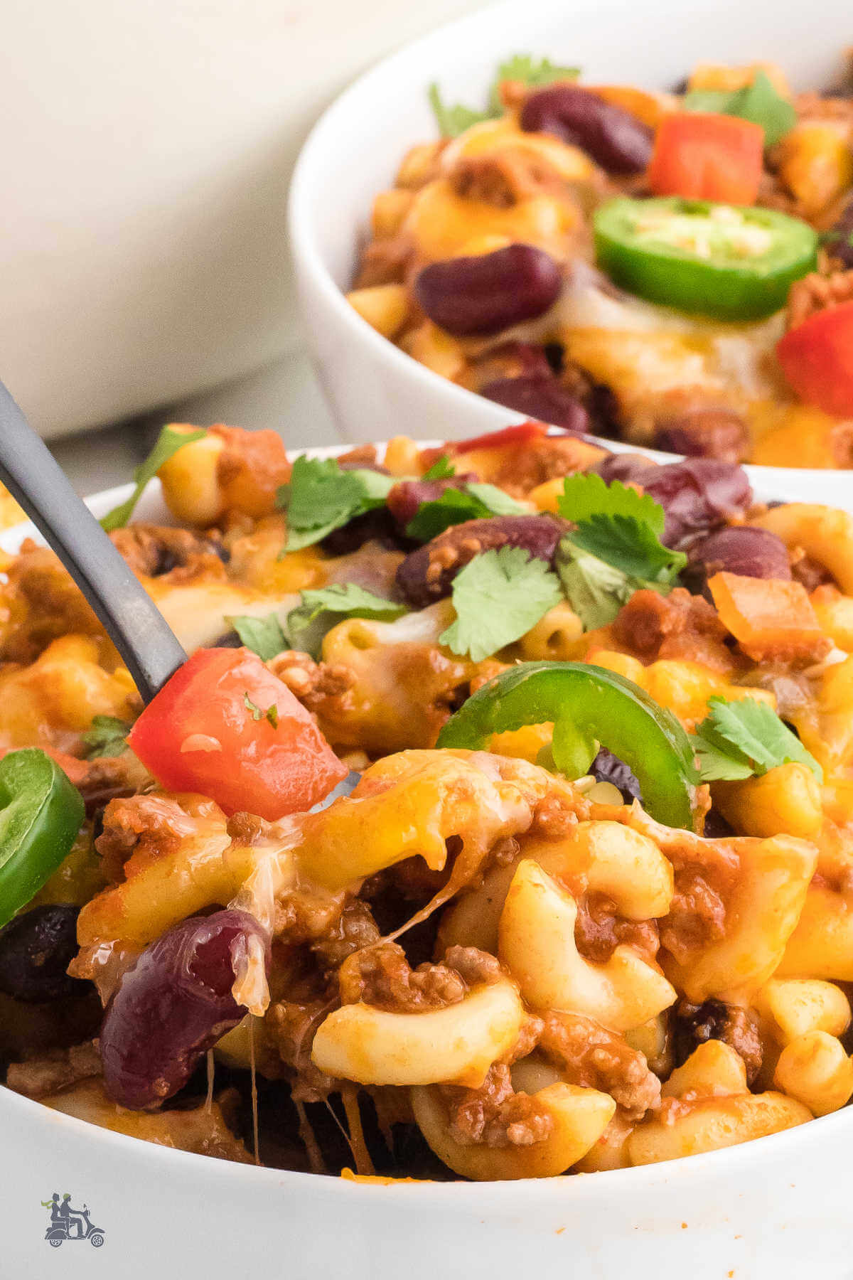 A spoon in a big bowl of chili macaroni and cheese with another bowl in the background. 