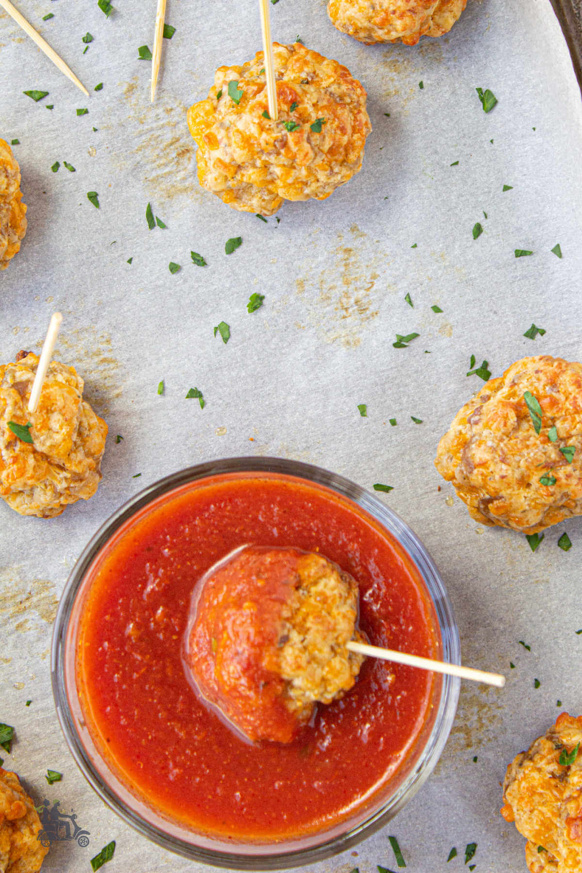 A sausage ball with a toothpick in the center for dipping into a bowl of marinara sauce. 