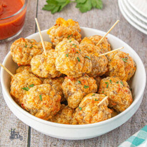 A sausage meatball pyramid in a white plate with the appetizers pierced with toothpicks.