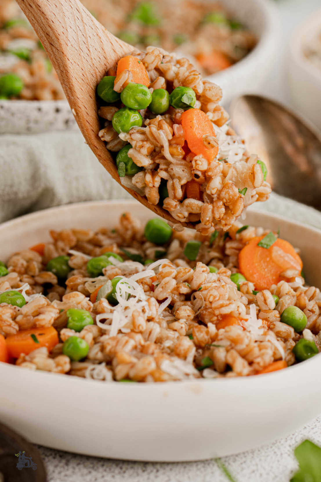 A wooden spoon serving a helping of cooked farro, peas, and carrots resembling Italy's classic dish of Risi e Bisi. 