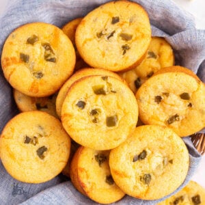 A blue tea towel lined wicker basket filled with cheesy jalapeno cornbread muffins made with Jiffy mix.