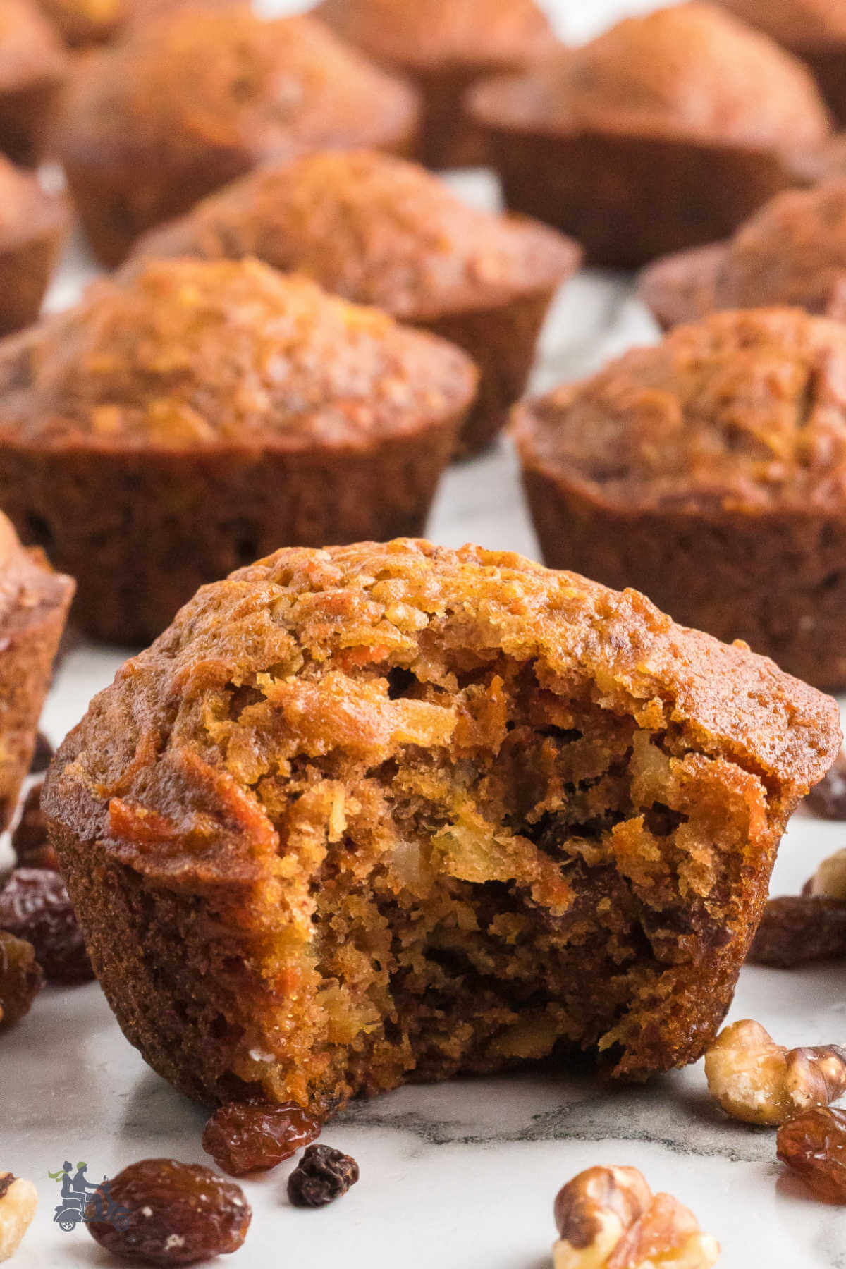 Carrot and pineapple Breakfast muffins on a white marble counter and one muffin has a bite taken from it. 