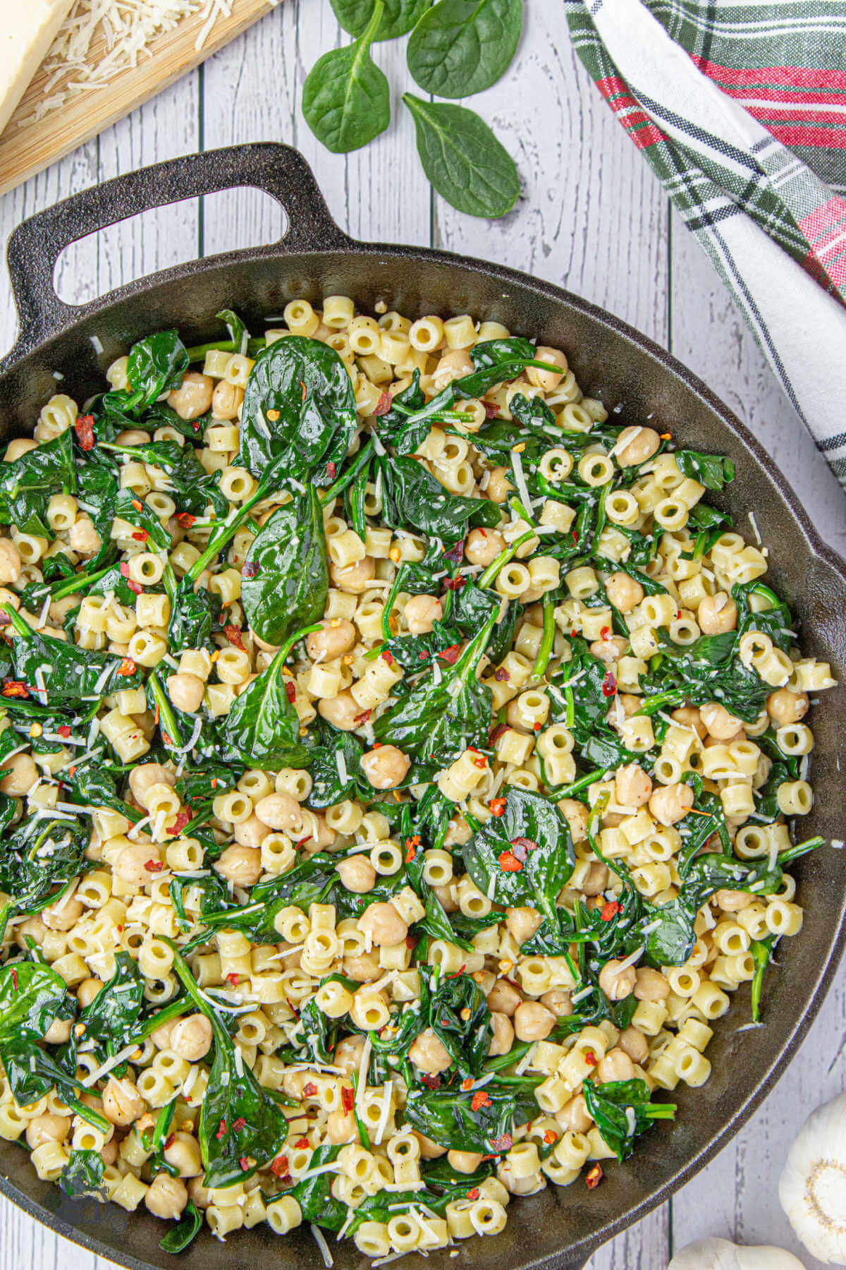 A black skillet filled with the finished recipe of Chickpeas and pasta with Spinach and red pepper flakes. 
