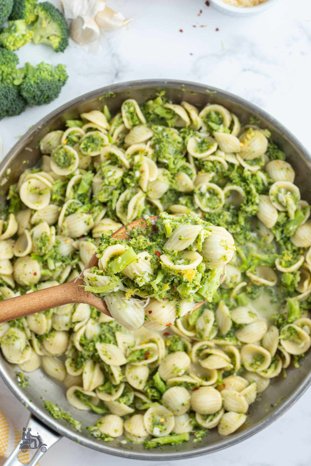 A steel skillet willed with orecchiette pasta with a wood spoon drawing up a scoop. 