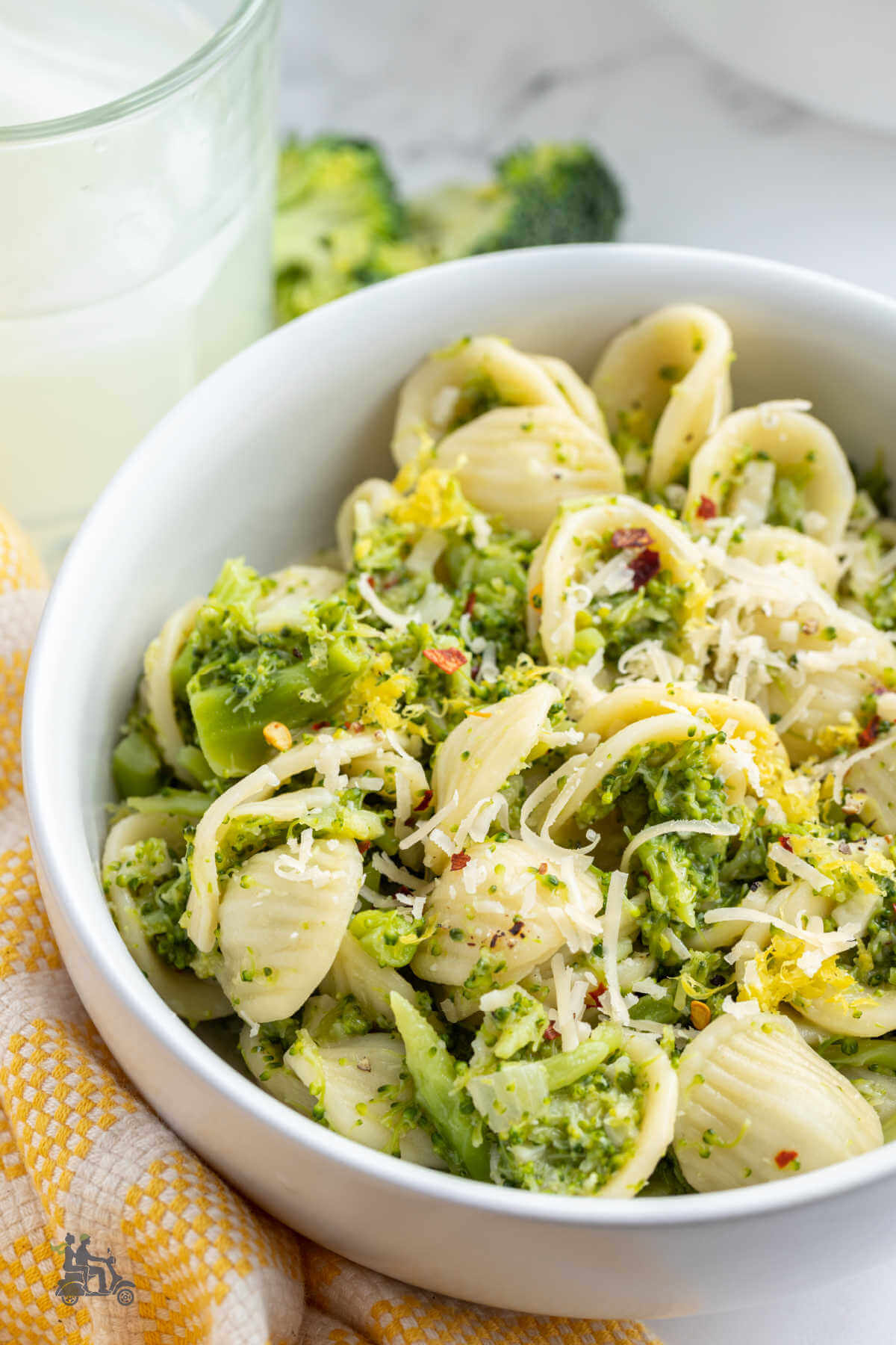 A white bowl filled with orecchiette pasta covered in creamy broccoli sauce and garnished with additional grated pecorino cheese and lemon zest. 