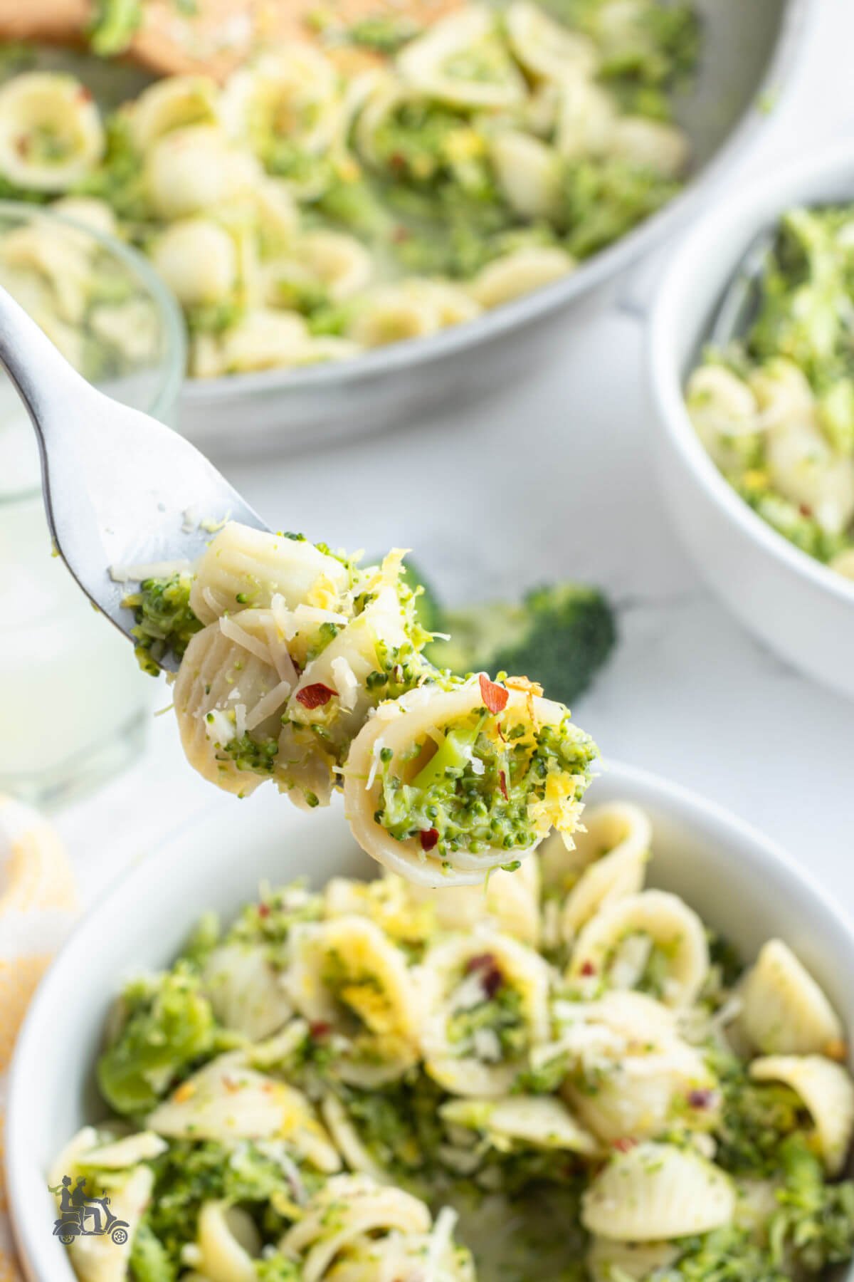 A fork holding a bite of orecchiette pasta with the broccoli sauce spiced with pepper flakes, lemon zest, and cheese. 