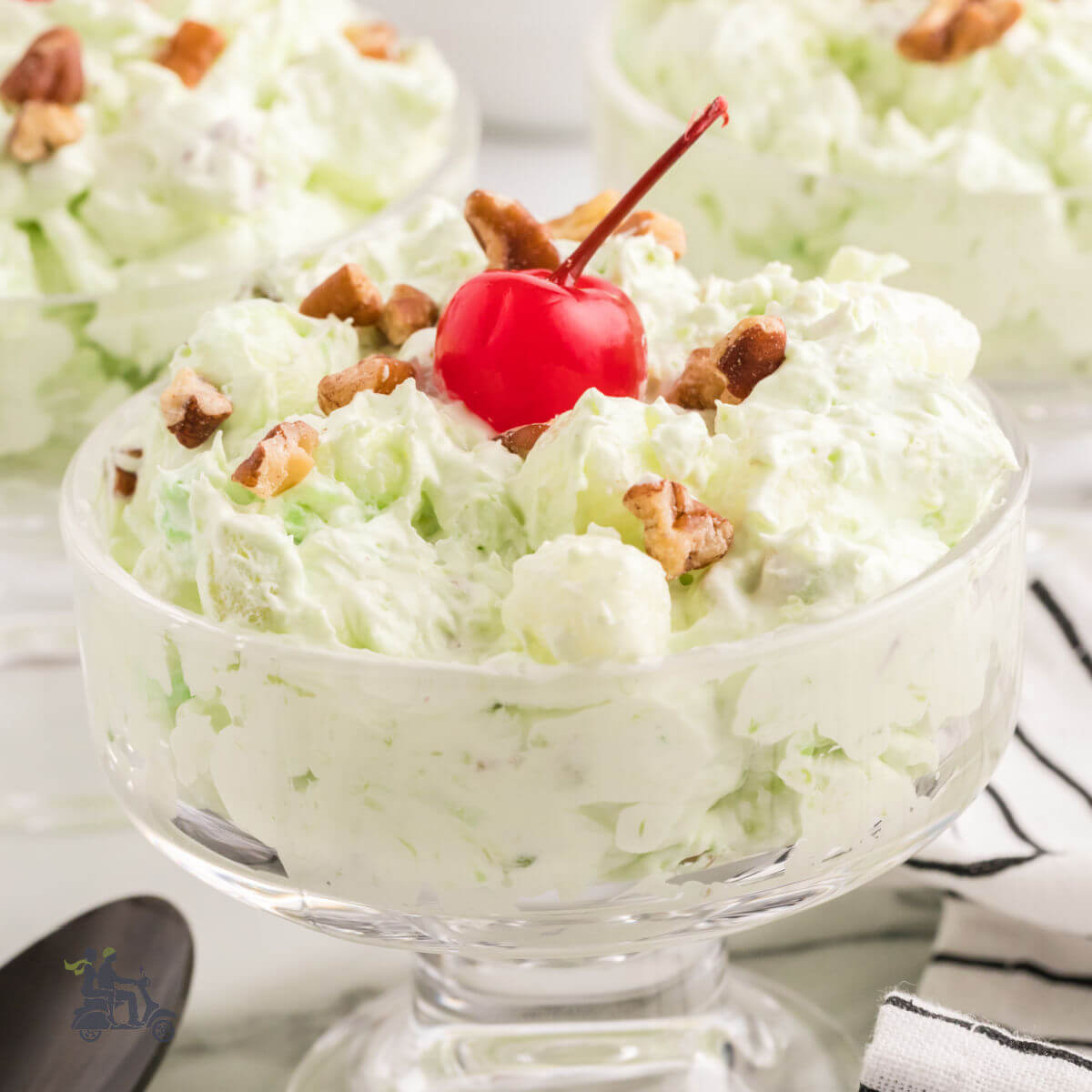 A glass goblet filled with Pistachio fluff or Watergate salad with maraschino cherry and pecans on top.