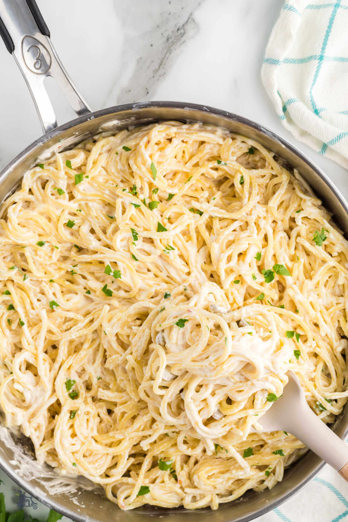 A skillet filled with pasta and cream cheese sauce with a wooden spoon stirring. 
