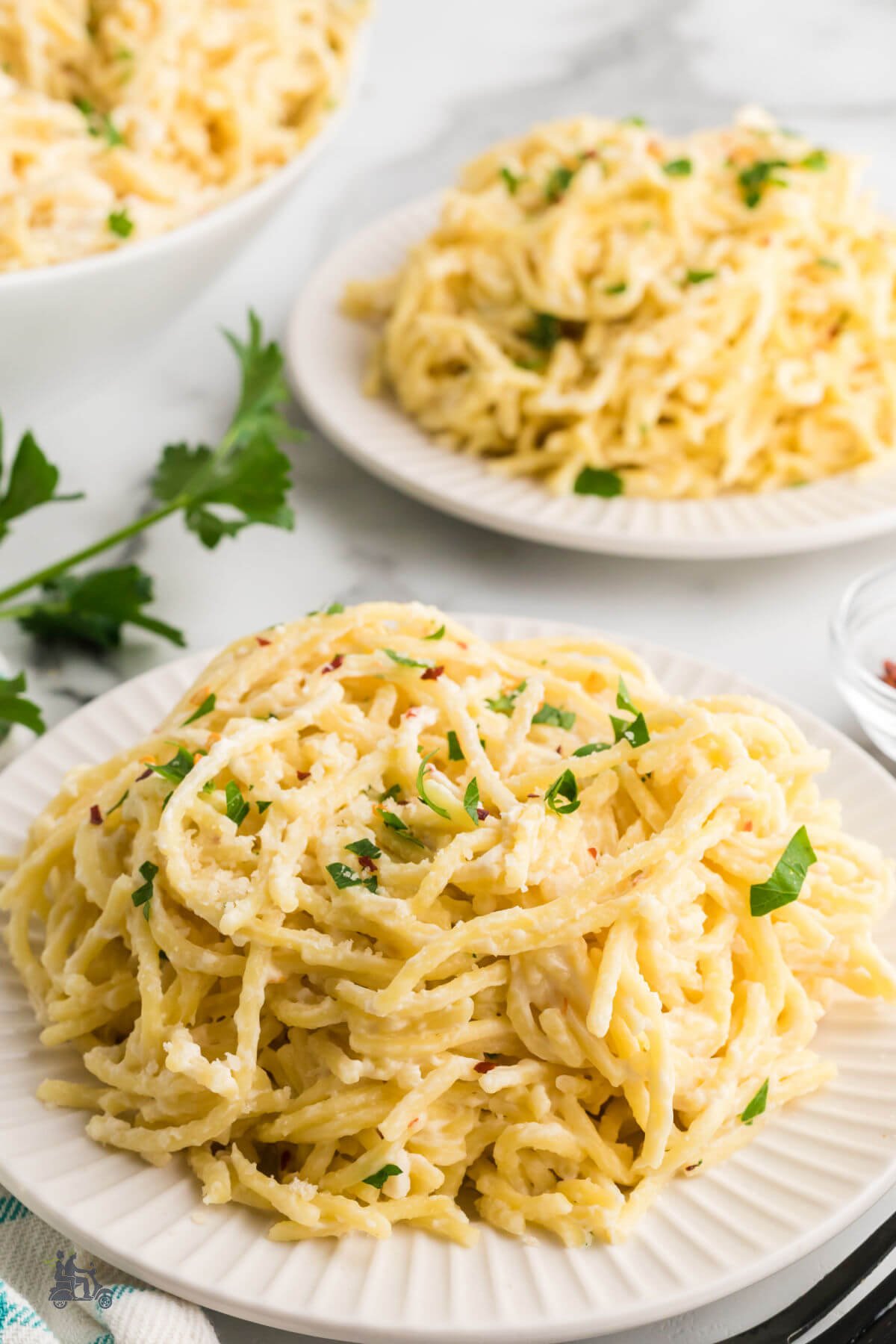 Two plates with servings of cream cheese spaghetti sprinkled with chopped parsley. 