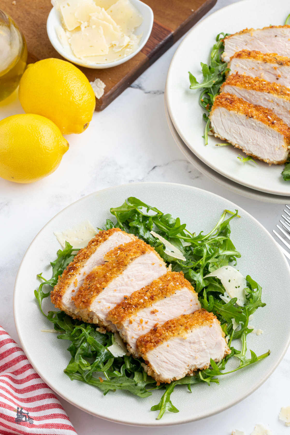 Two plates with a servings of the breaded  fried pork on a bed of arugula salad. 