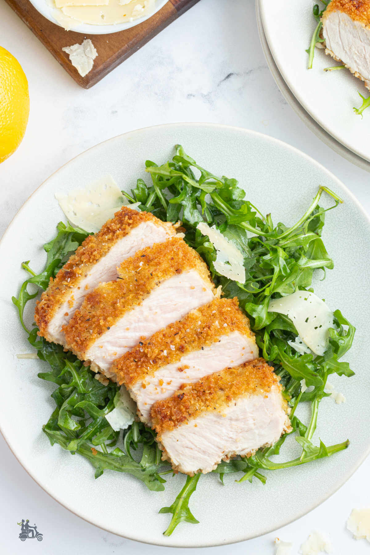 Overhead view of the pan-fried pork chops breaded in crispy breadcrumbs and served over arugula salad tossed with shaved parmesan and lemon vinaigrette. 