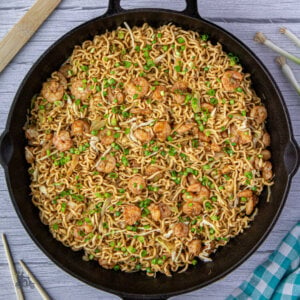 A black skillet with teriyaki noodles sauteed with shrimp and sprinkled with green onions.