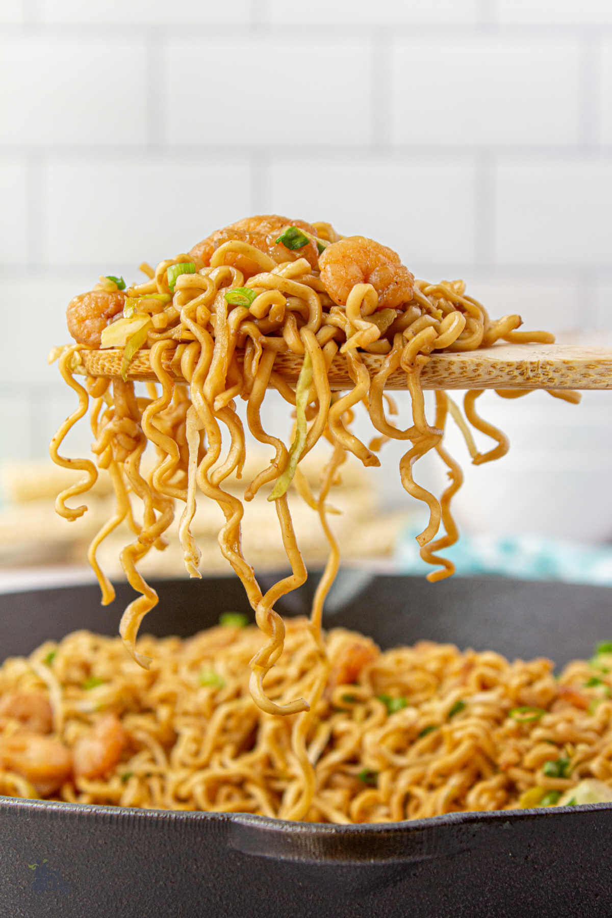 A wooden spoon holding a portion of teriyaki noodles with shrimp. 