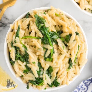 A white bowl filled with orzo pasta made with lemon and spinach in a creamy wine parmesan sauce.