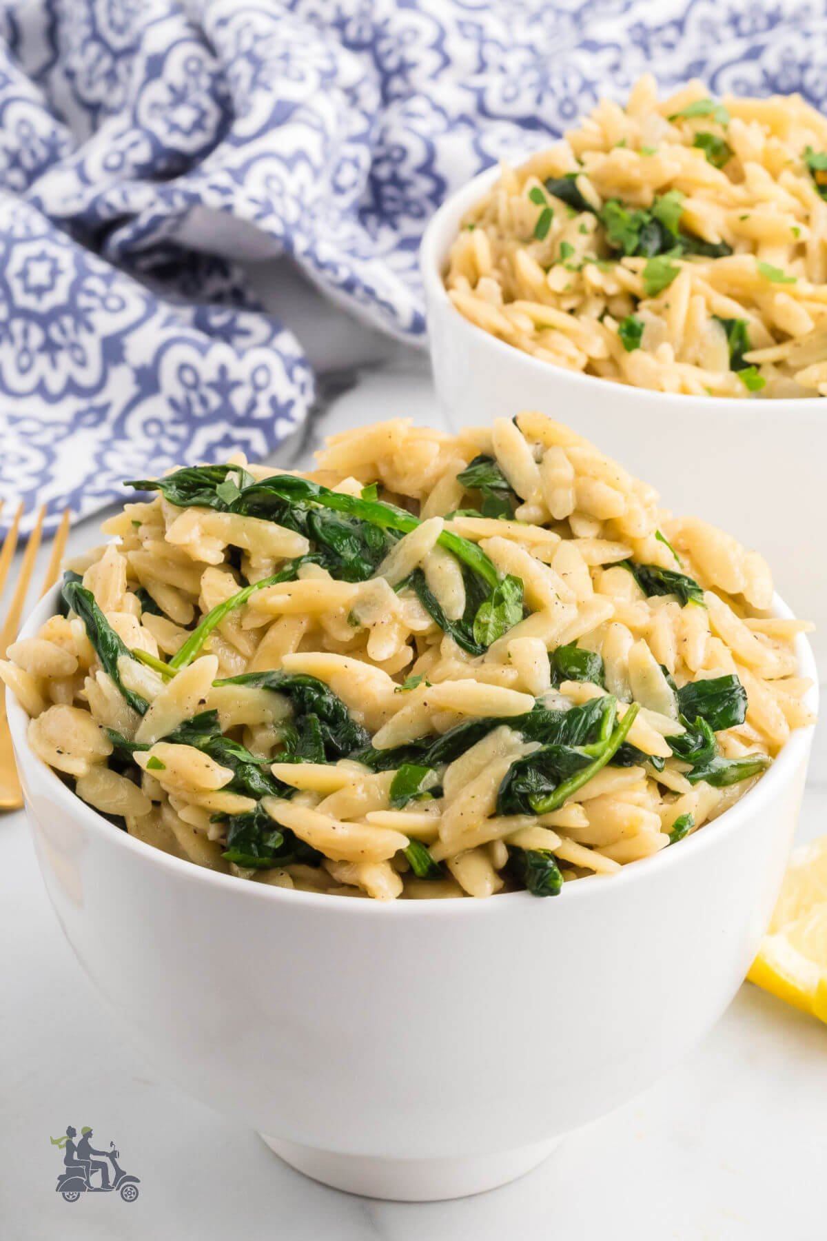Two white bowls filled with risoni pasta made with lemon and spinach and served in a creamy wine parmesan sauce. 