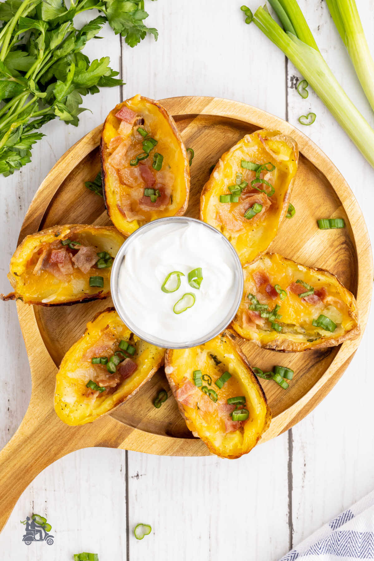 A wooden serving tray with crispy baked potato skins made with cheese, bacon and green onions.