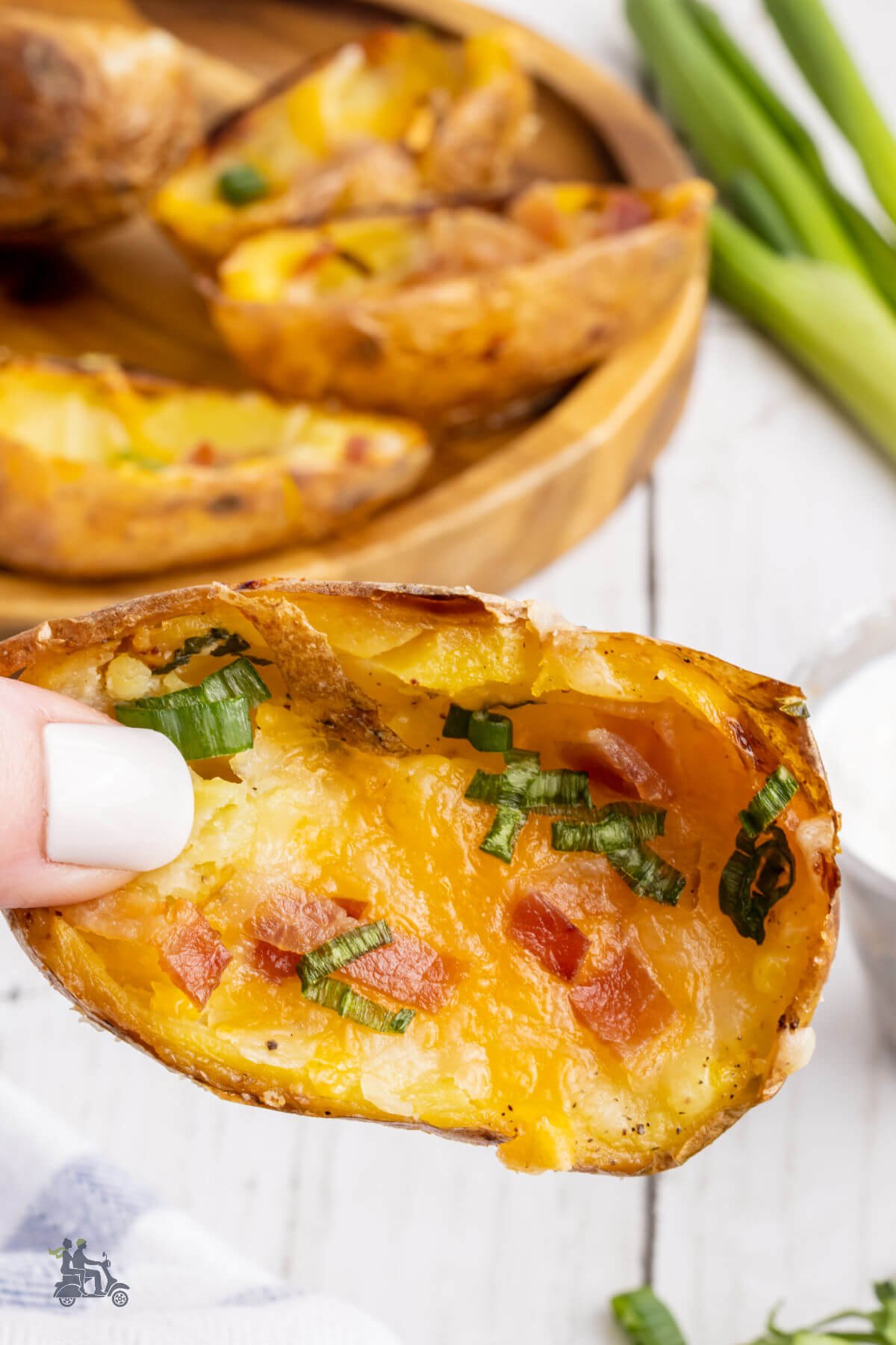 A hand grabbing a baked potato skin half that's been made with cheese, bacon and sprinkled with green onions. 