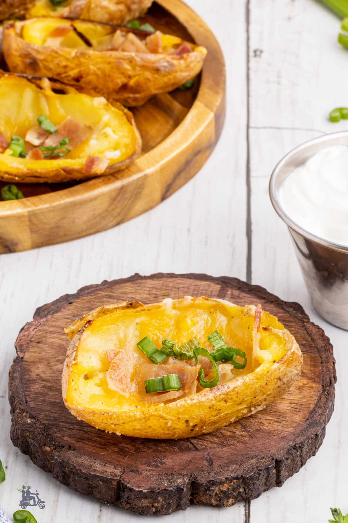 A wooden serving round holding half of a potato skin that has been baked with melted cheese, bacon, and green onion. 