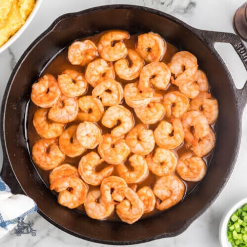 Black cast iron skillet holding the bbq shrimp recipe that's completed.