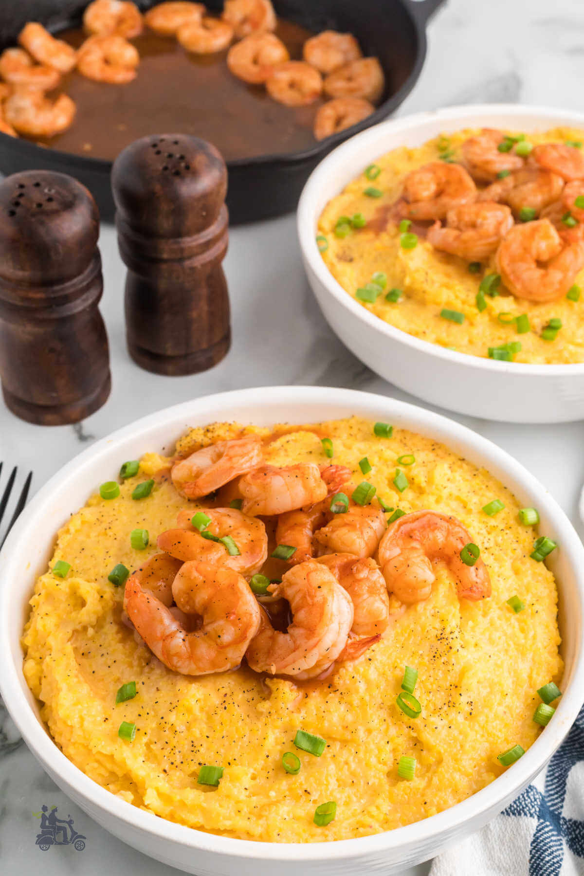 Two white bowls filled with cheesy corn grits topped with barbecue prawns and sprinkled with slivered green onions.