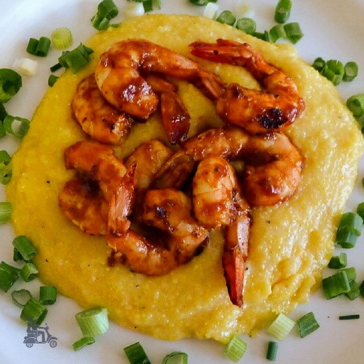 BBQ Shrimp on top of cheesy corn grits with a sprinkle of green onions surrounding the dish. 