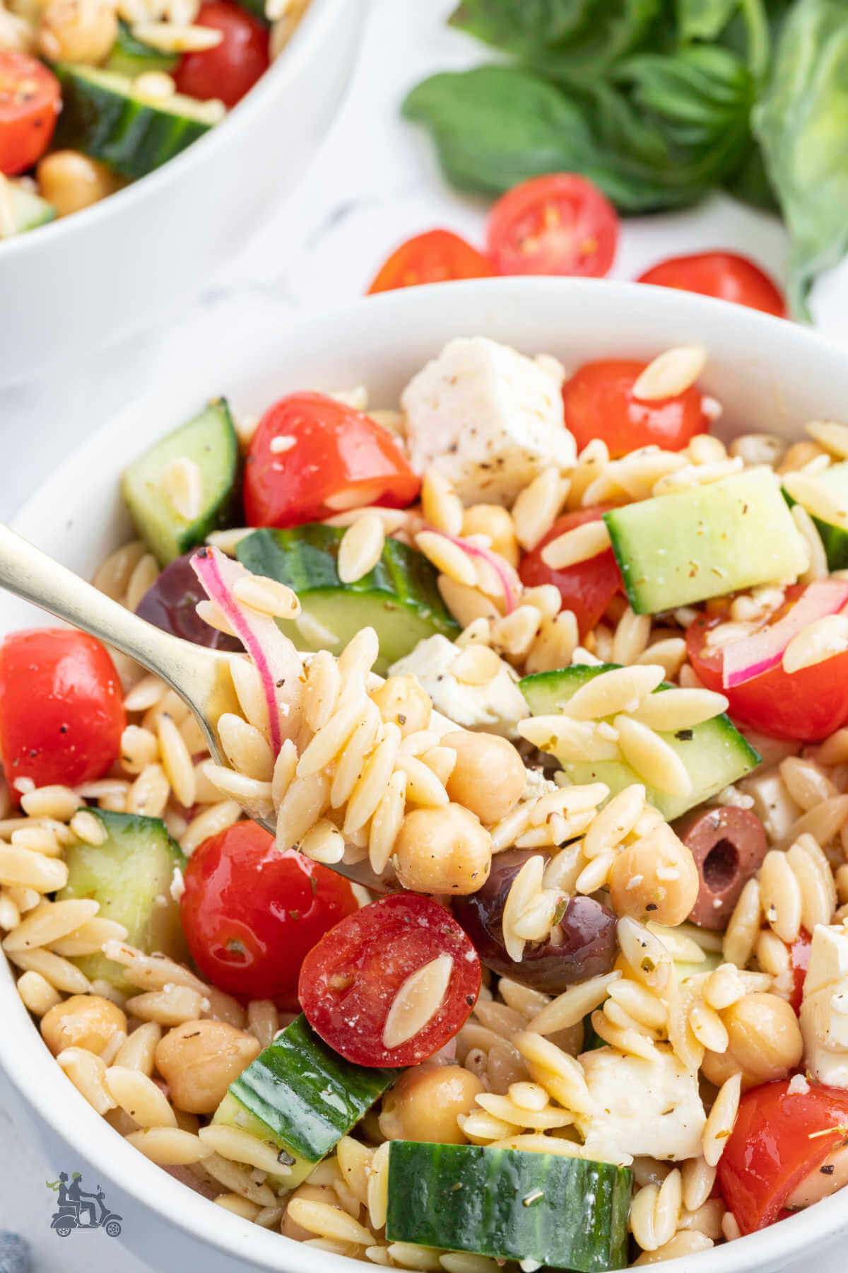 A white serving bowl holding a recipe of Greek Orzo pasta salad. 