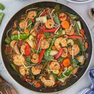 A skillet with shrimp chop suey with sauce featuring red bell pepper slices, green snow peas, and more Asian style vegetables.