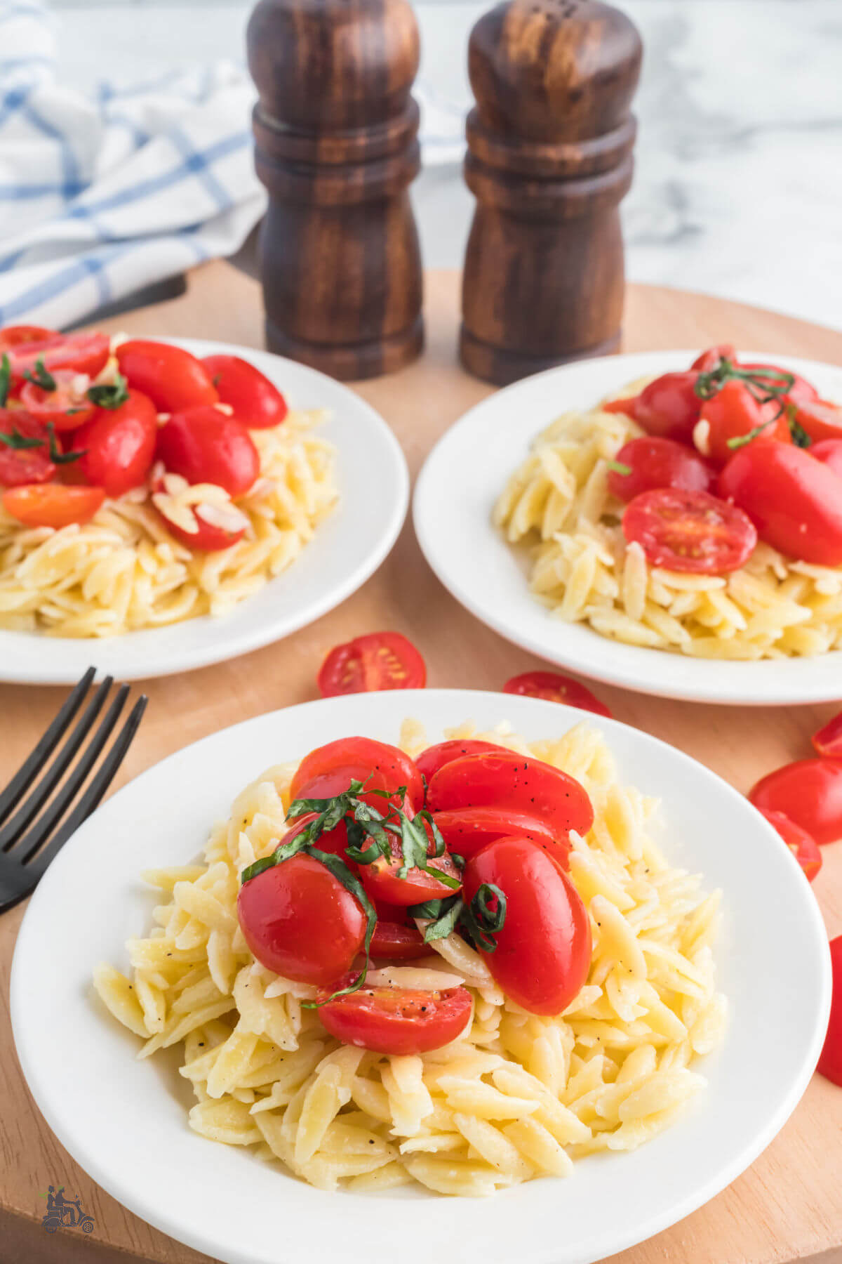 White plates filled with creamy orzo pasta topped with marinated grape tomatoes.