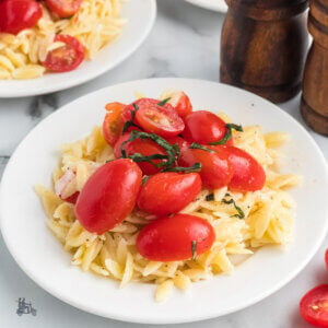 A plate piled with creamy orzo and topped with marinated tomatoes on top.