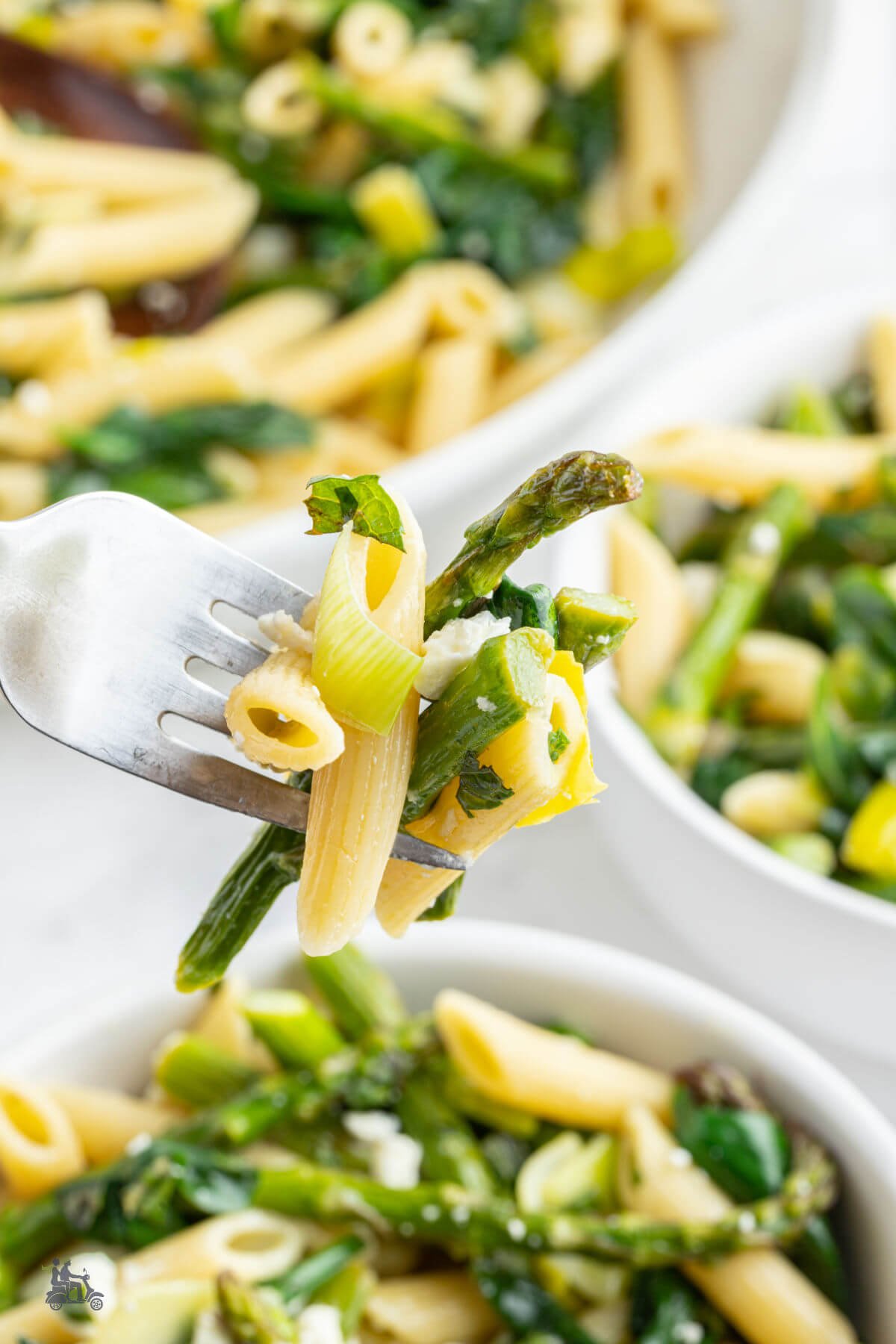 A fork holding a bite of pasta, asparagus, spinach, and leek from the Primavera pasta recipe. 