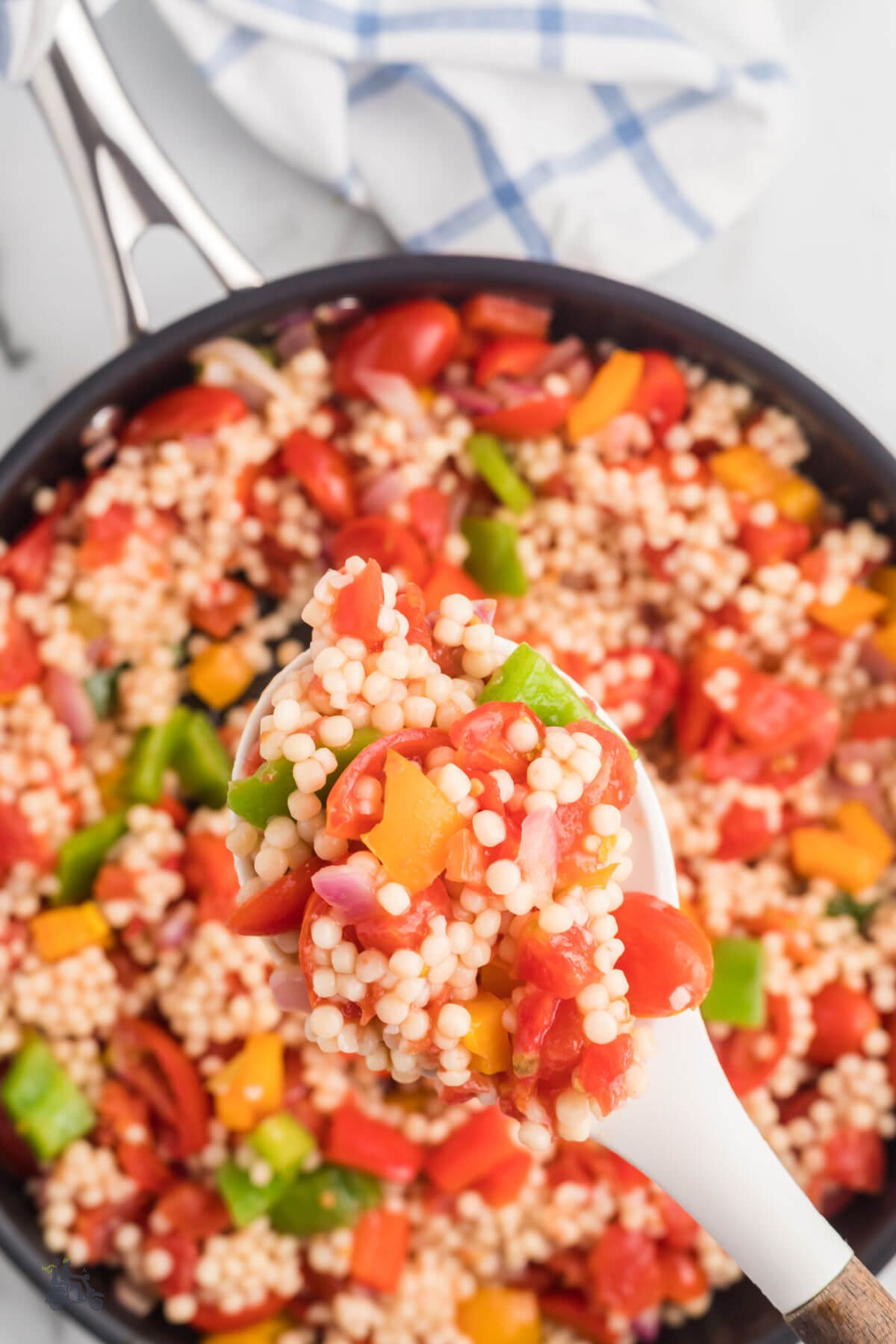 A closeup of a spoon holding a helping of Israeli couscous sautéed with colored bell peppers, onion, and tomatoes. 