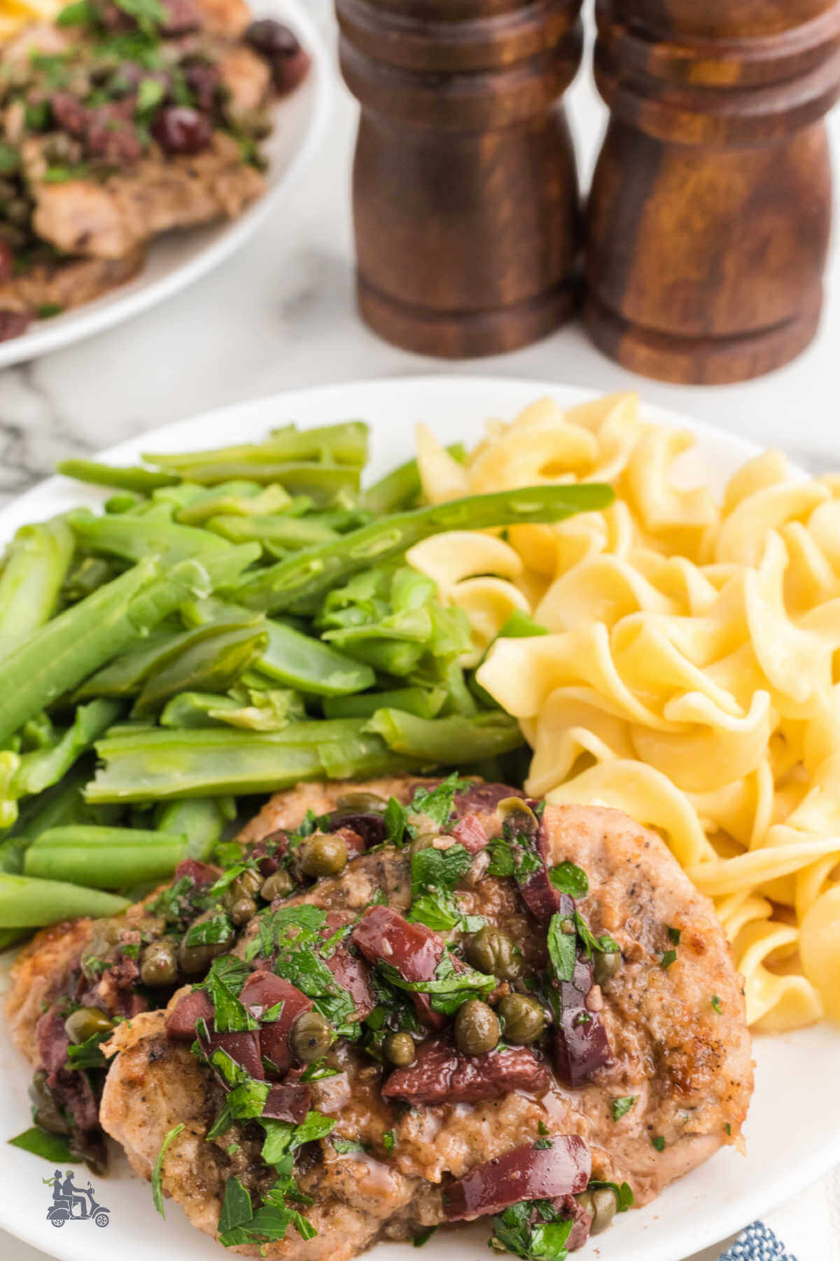 Pork Tenderloin Medallions with an Olive Caper Sauce on a plate with egg noodles and French style green beans.