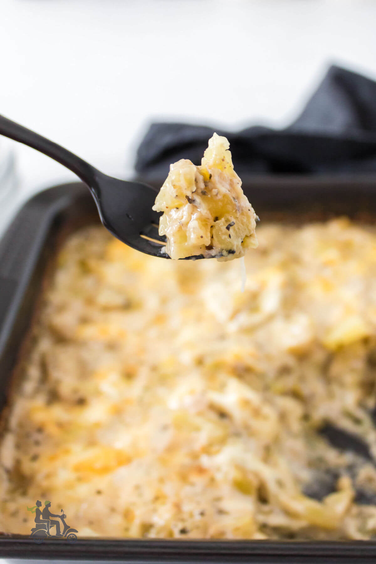 Fork holding a bite of diced potatoes made au gratin style. 